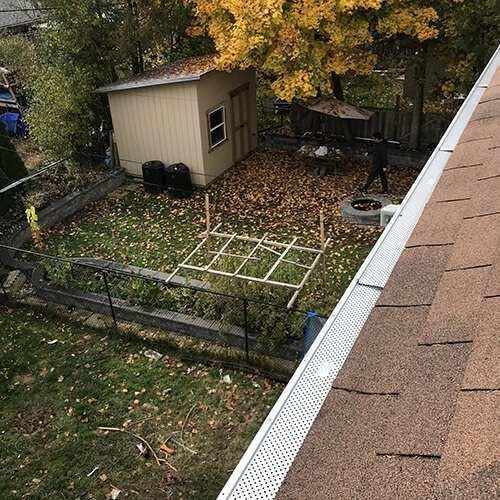Top-down view of a Toronto roof with a clean eavestrough, with a perforated aluminum gutter guard placed on the shingles, ready for installation.