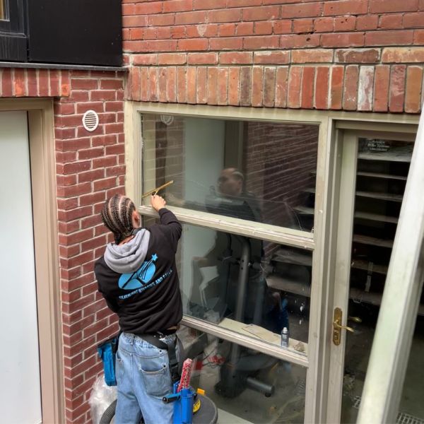 A professional Silverlight technician using a hand-held squeegee to meticulously clean an exterior ground-level window of a red brick home in Newmarket, ON.