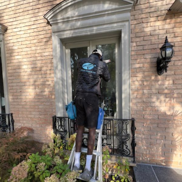 A professional Silverlight Windows and Eaves technician performing detailed window cleaning on a classic, traditional brick home entrance in Lawrence Park.