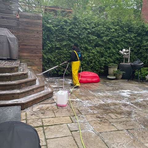 Stafan Lionel power washing a stone patio and wooden deck stairs at a residential property in Toronto.