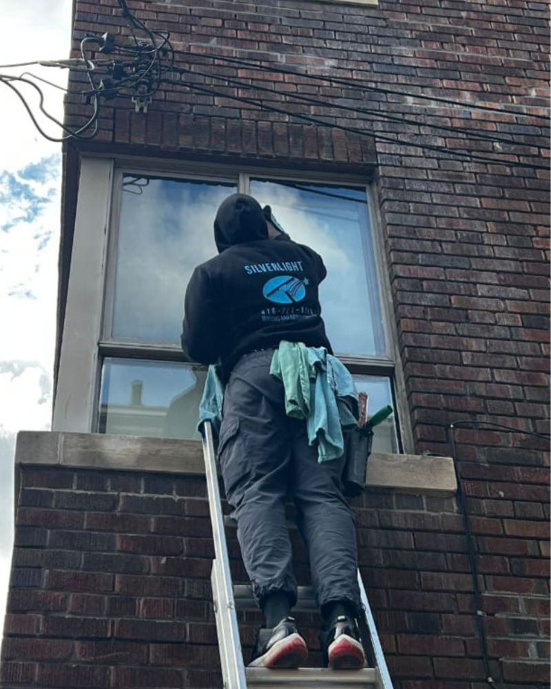 Silverlight technician performing ladder-based window cleaning on a brick home in Etobicoke.